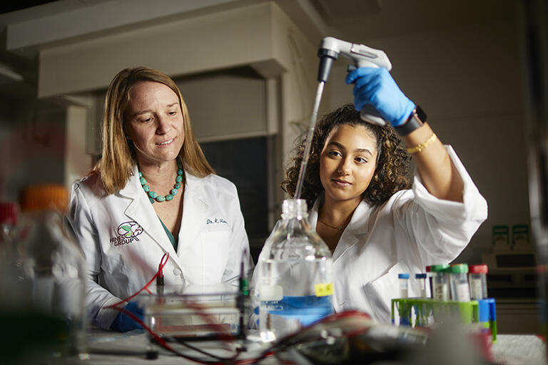 Two lab workers in white coats working with various fluids and lab equipment