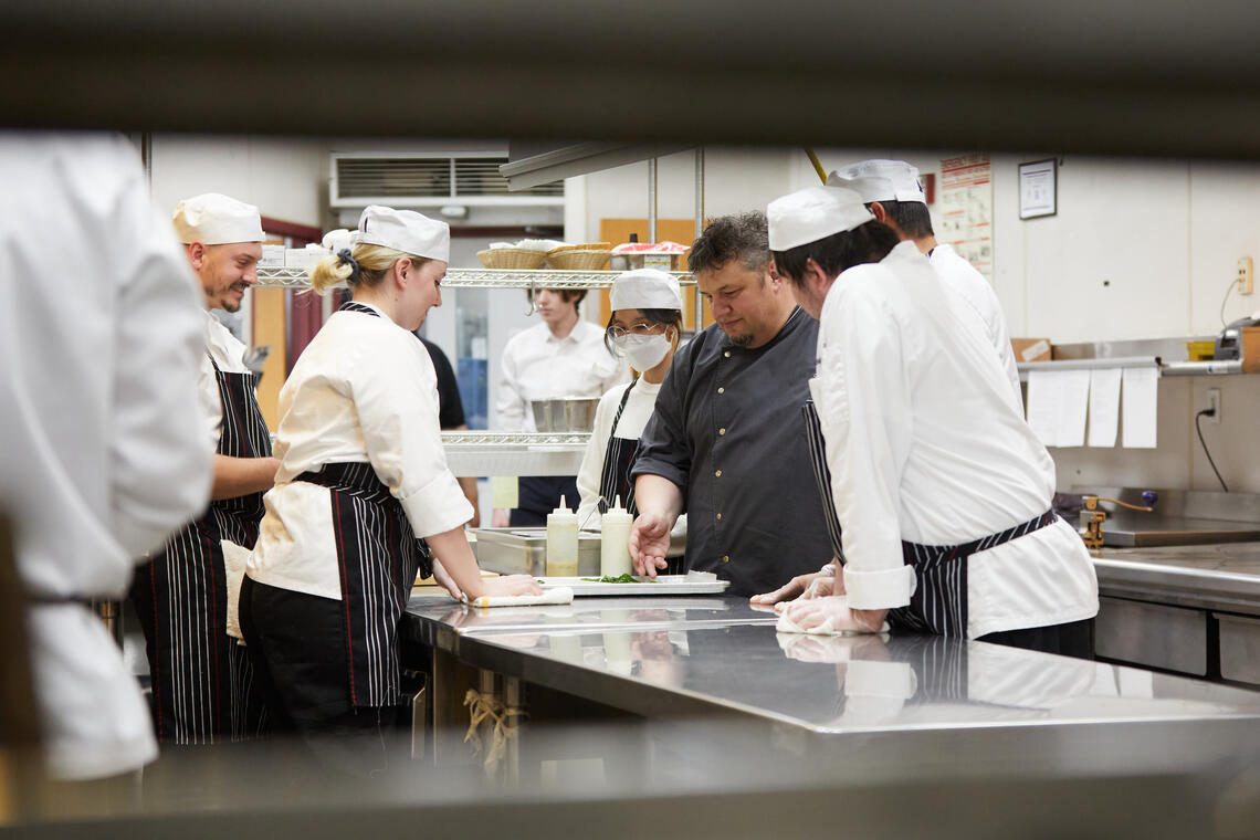 Chef Chris Lindsay shows hospitality students how to plate food in the kitchen