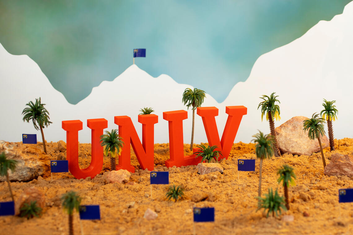 UNLV letters in desert scene with sand, palm trees, rocks, Nevada flag and mountains