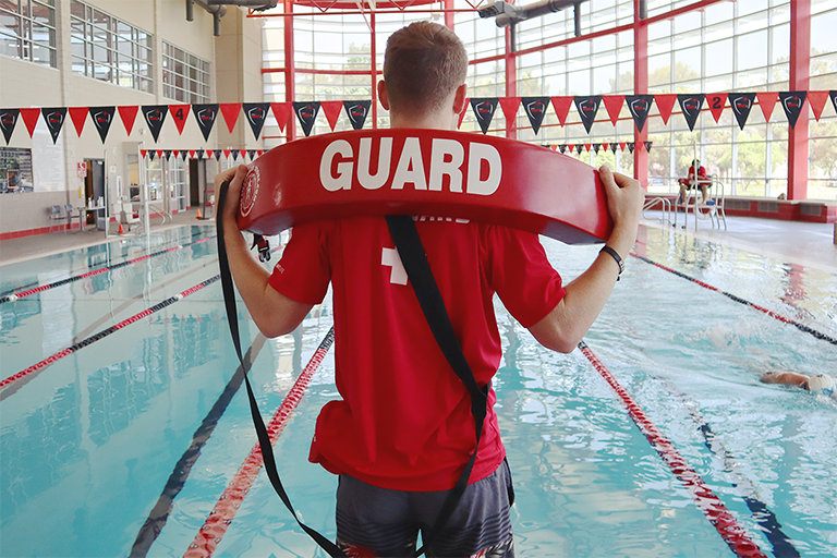 lifeguard facing the pool with a red float 