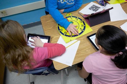 Two children sitting at a table with a learning clock