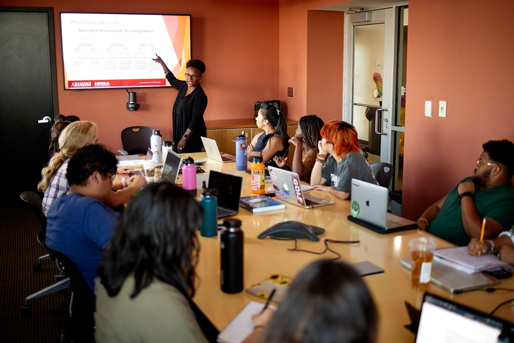People in a meeting room with woman pointing at TV