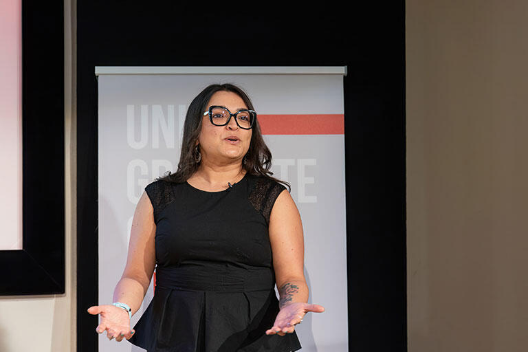 A woman wearing a black dress and glasses talking