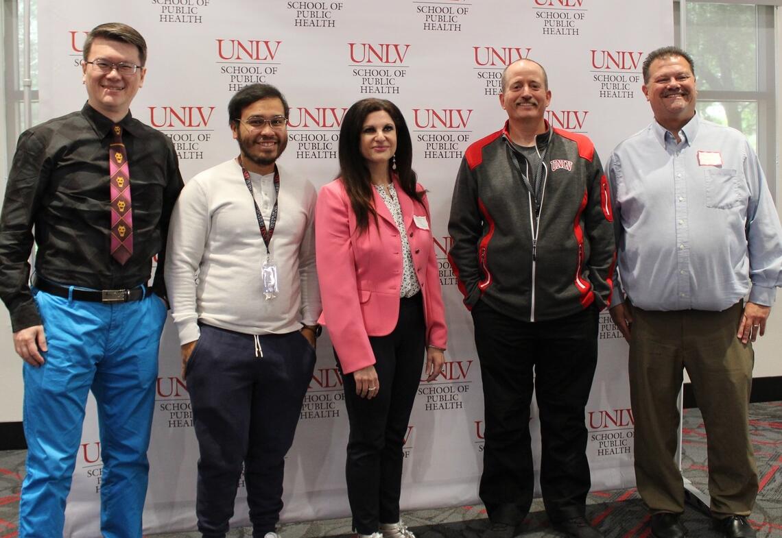 group of people posing for a photo in front of a UNLV backdrop