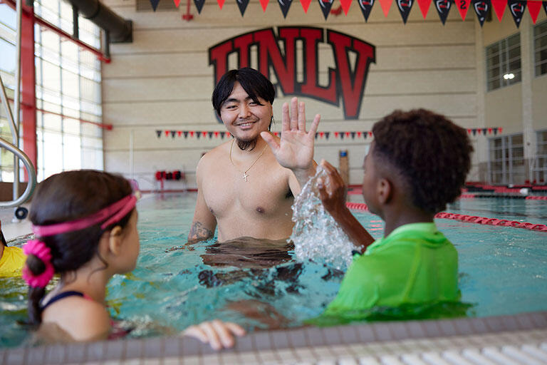 A man and two children in a large pool waving to each other