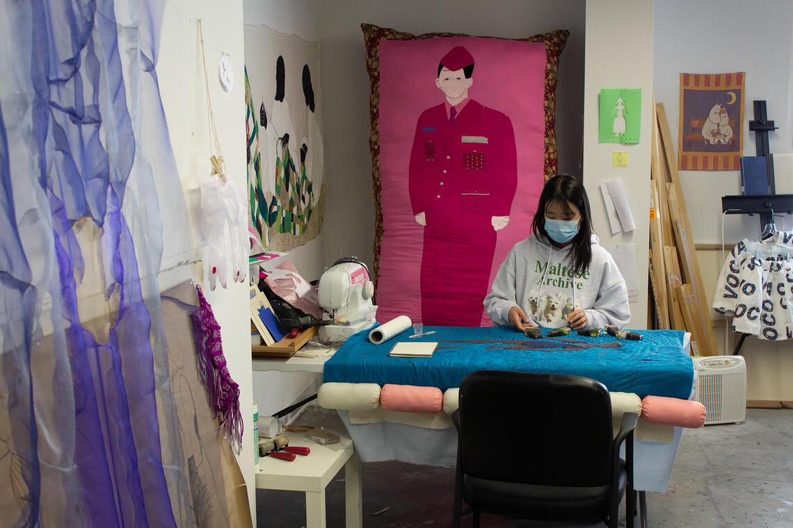 Student on a work table with different mediums of art surrounded