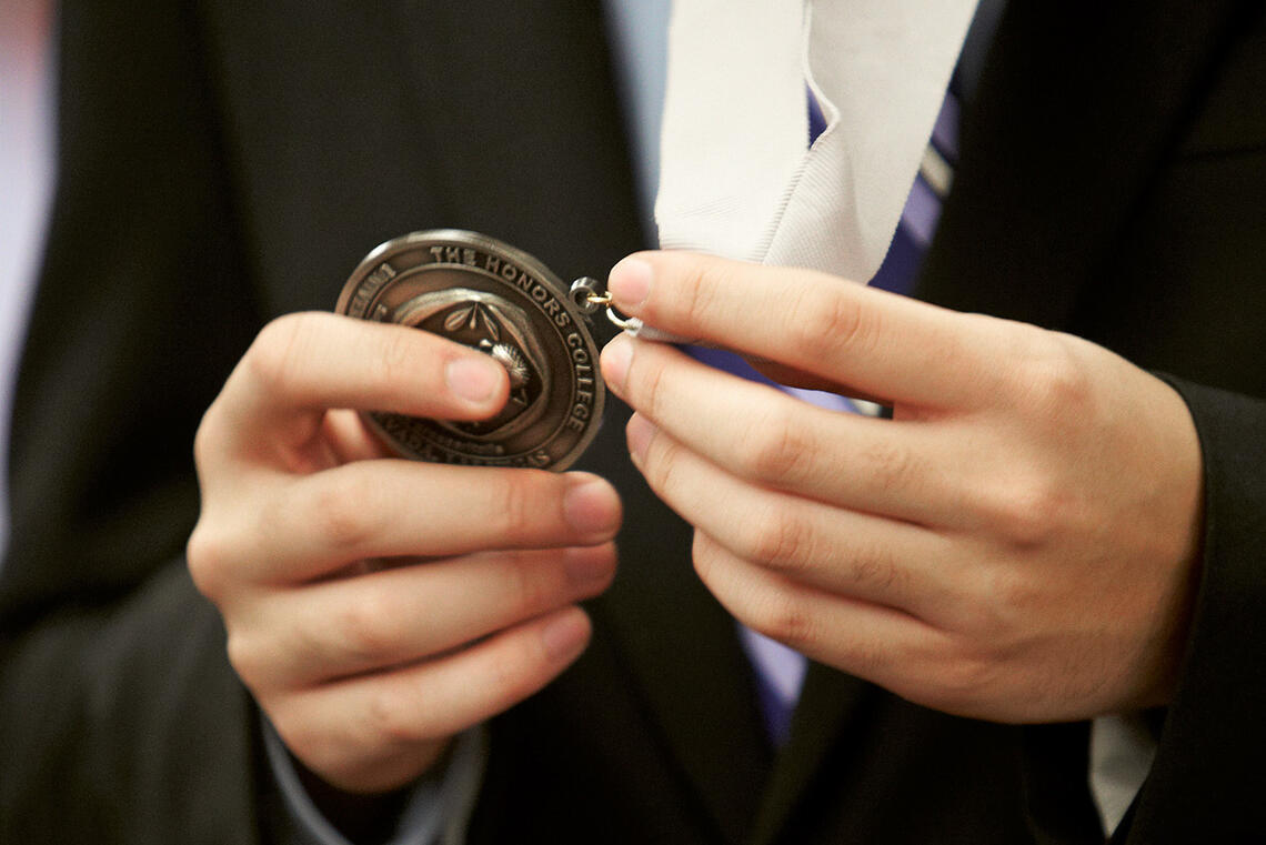 a pair of hands holding a brown medallion with 'Honors' etched on it