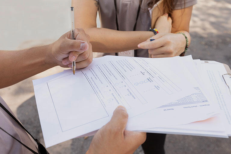 A person filling out a form with another person standing next to them.