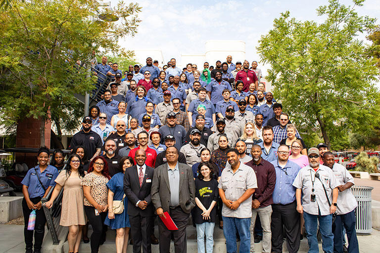A team photo of the Facilities Management staff members standing on a staircase outside of the Student Union