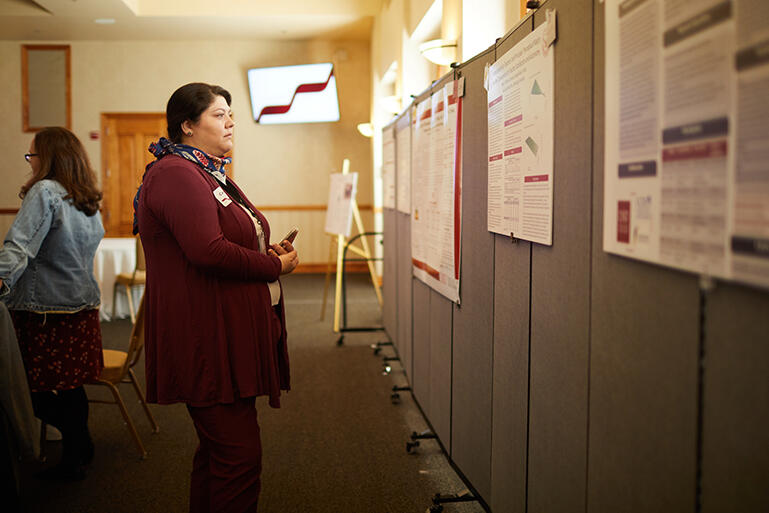 two women standing in a room and one of them is looking at a wall full of research posters