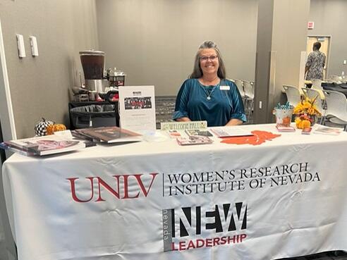 Woman sitting behind a table with cloth that says "Women's Research Institute of Nevada"