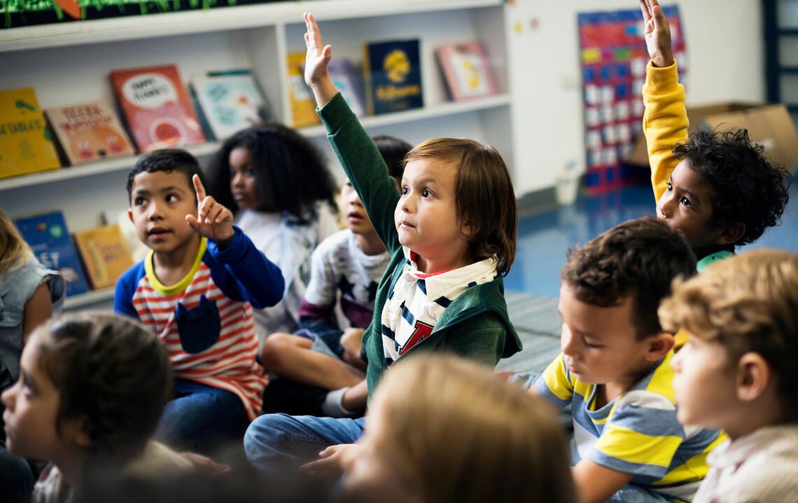 children gathered on the floor and one child in the center raising their hand