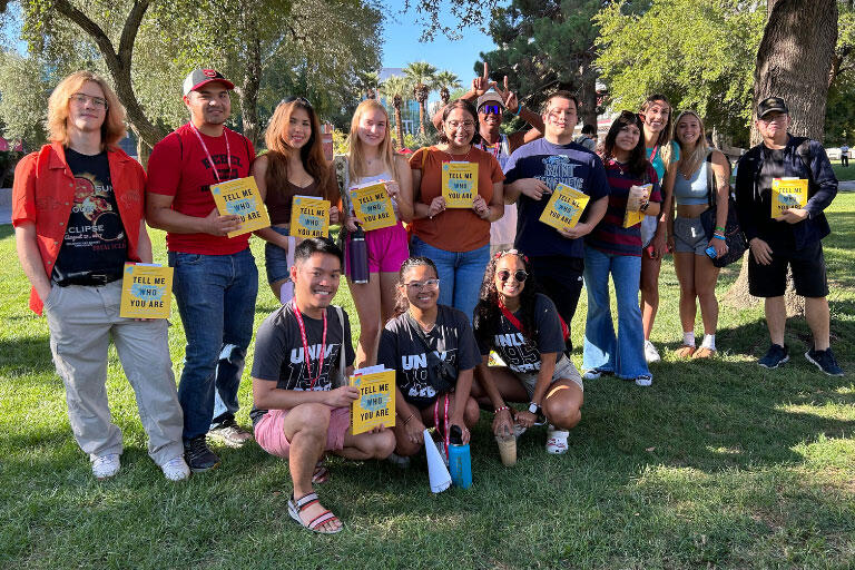 A group of people holding up a book titled Tell Me Who You Are