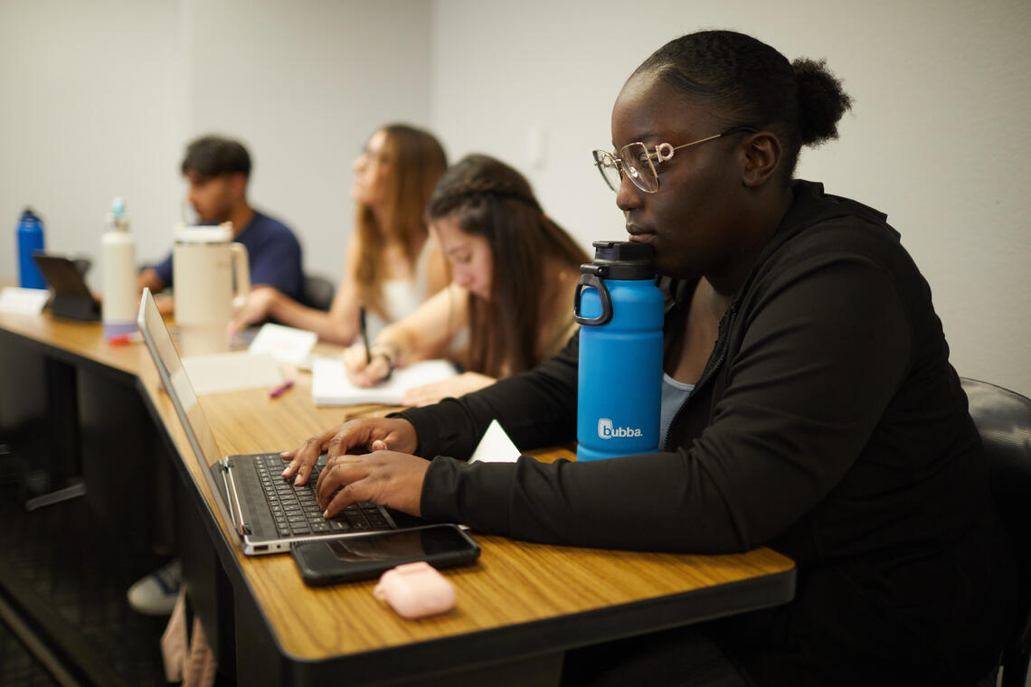 Student resting their chin on a water bottle while in front of a laptop