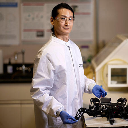 A portrait of person wearing a white coat and protective glasses in a lab