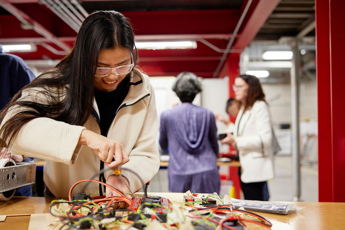 A student wearing safety googles and a white lab working on a project