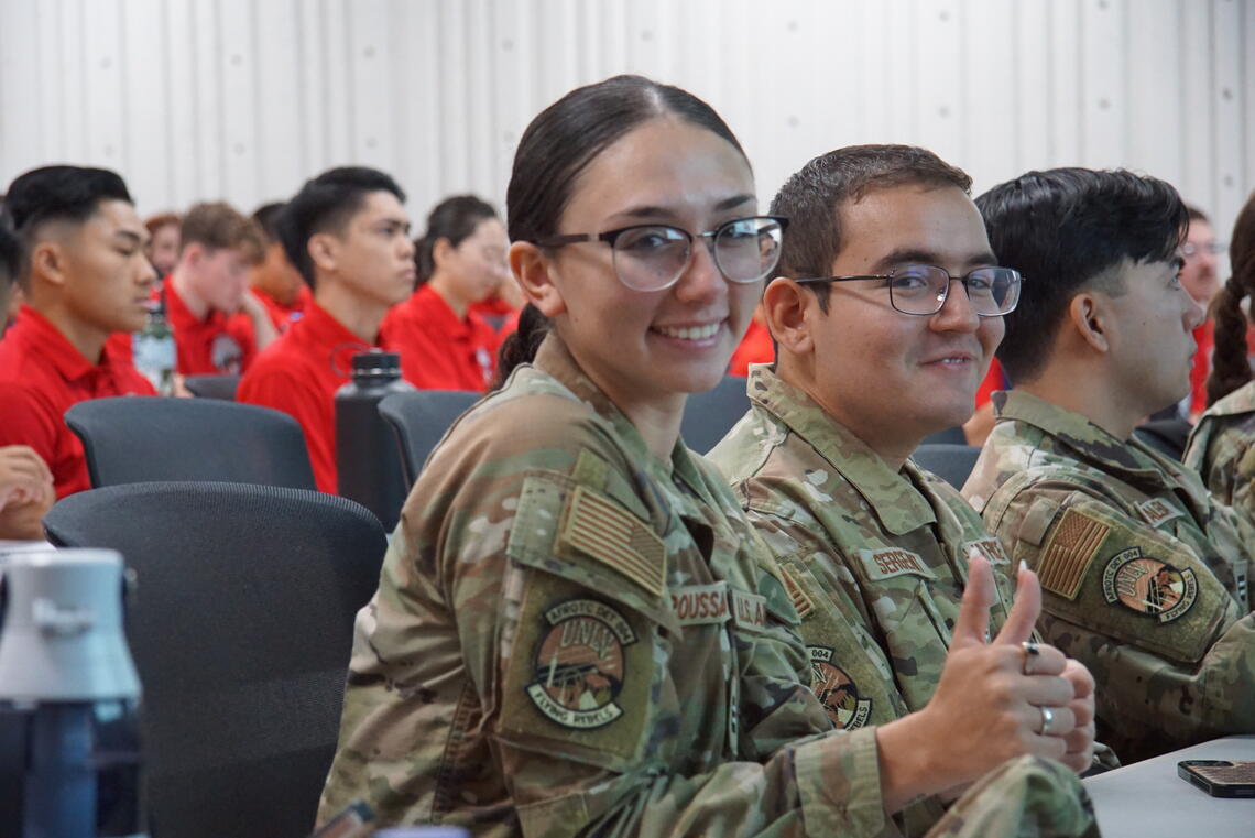 Room full of ROTC cadets. One is smiling at the camera with a thumbs up.