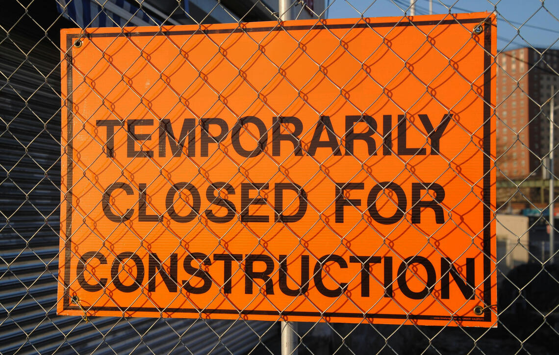 Orange sign on fence that reads: Temporarily Closed For Construction