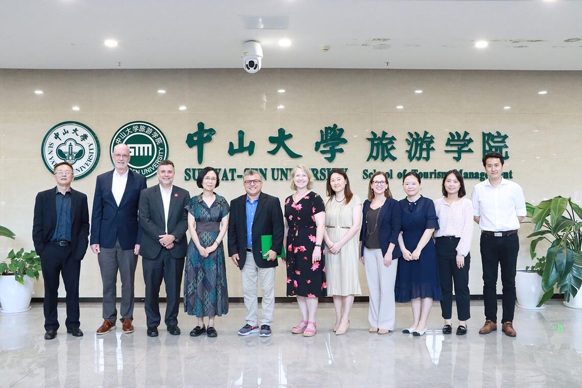 A group of twelve people stands in a row inside a building lobby with a polished floor.