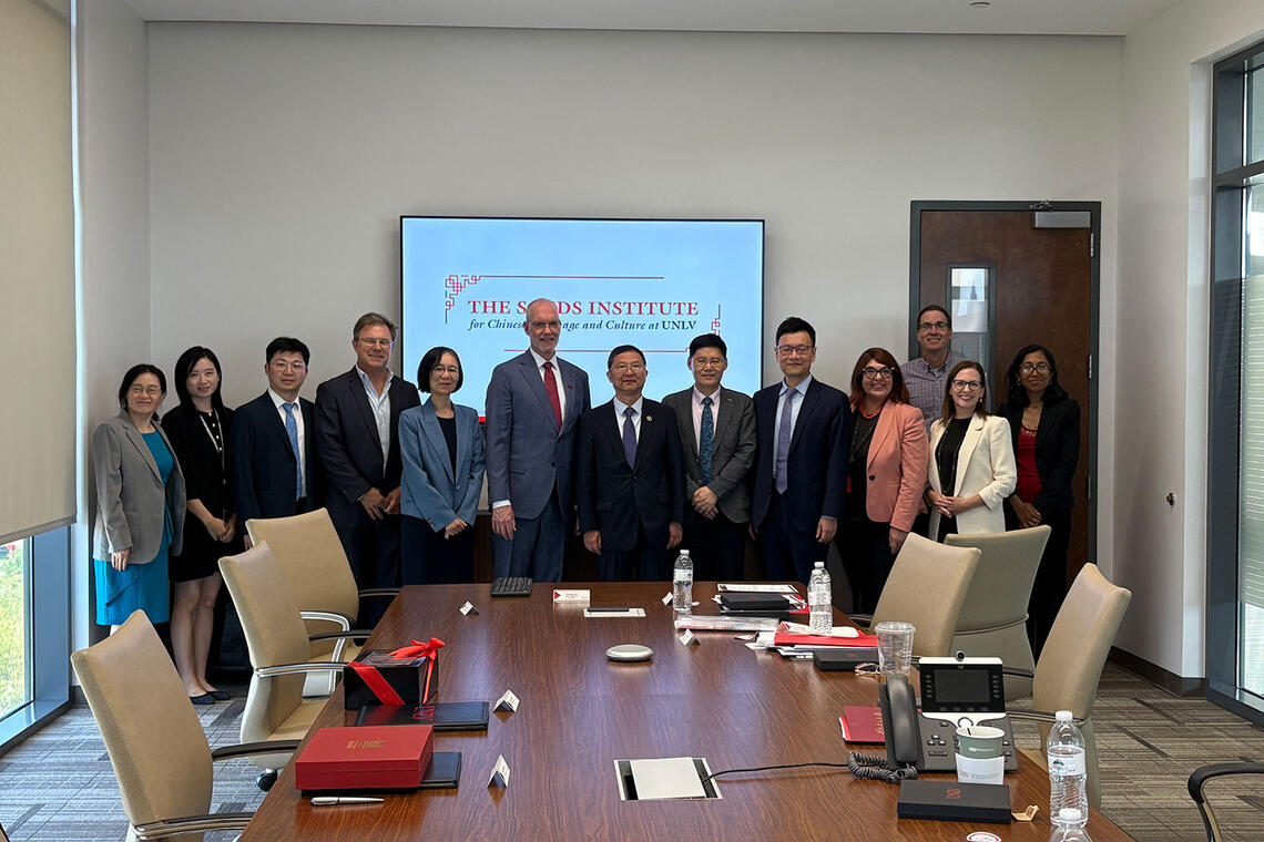 A group of thirteen people in a row poses in a meeting room.