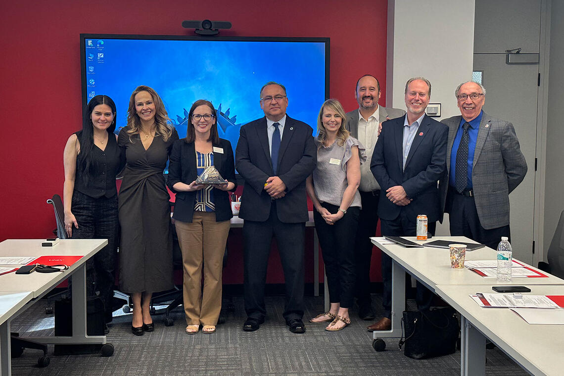 A group of eight people poses together in a conference room.