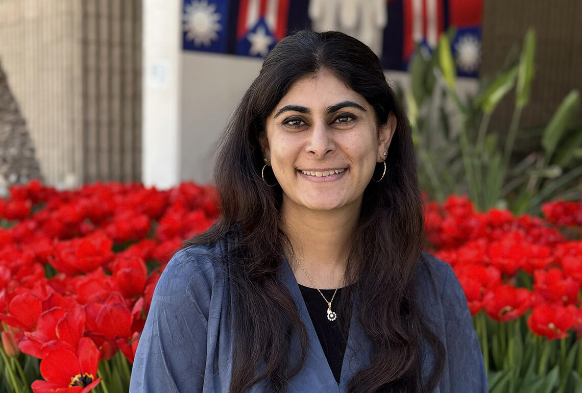A woman smiling outside in front of red flowers