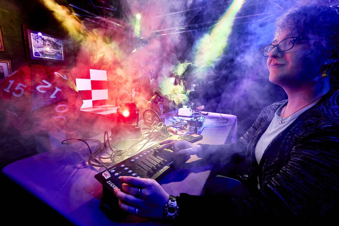 A student sits at a console while bright colorful stage lights and fog surround them