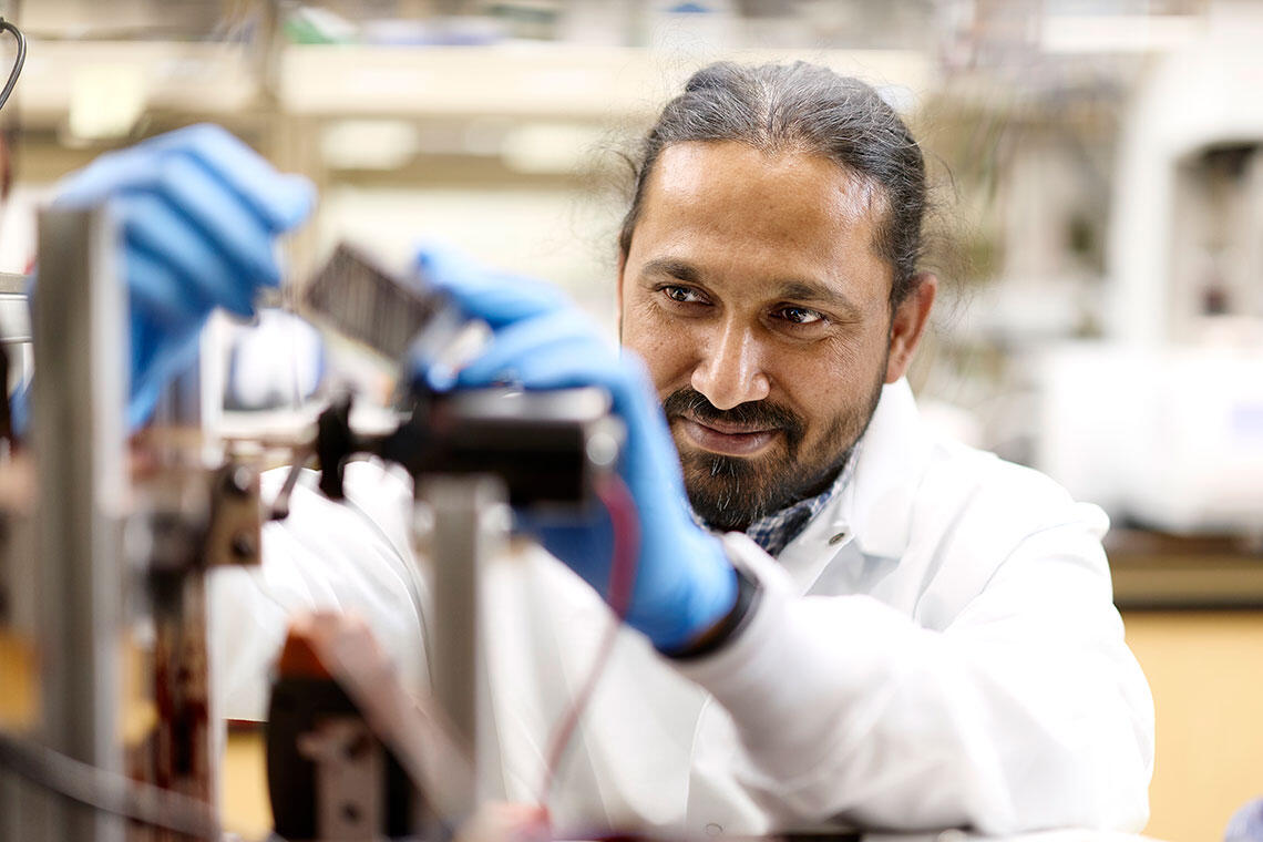 A scientist wearing a white lab coat and blue gloves adjusts equipment in a lab