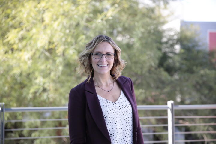 Color photograph of Shae Deschutter standing outdoors on a balcony in front of a tree