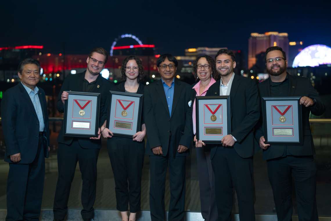 Seven people pose for a photo with the Las Vegas Strip in the background with four students holding awards