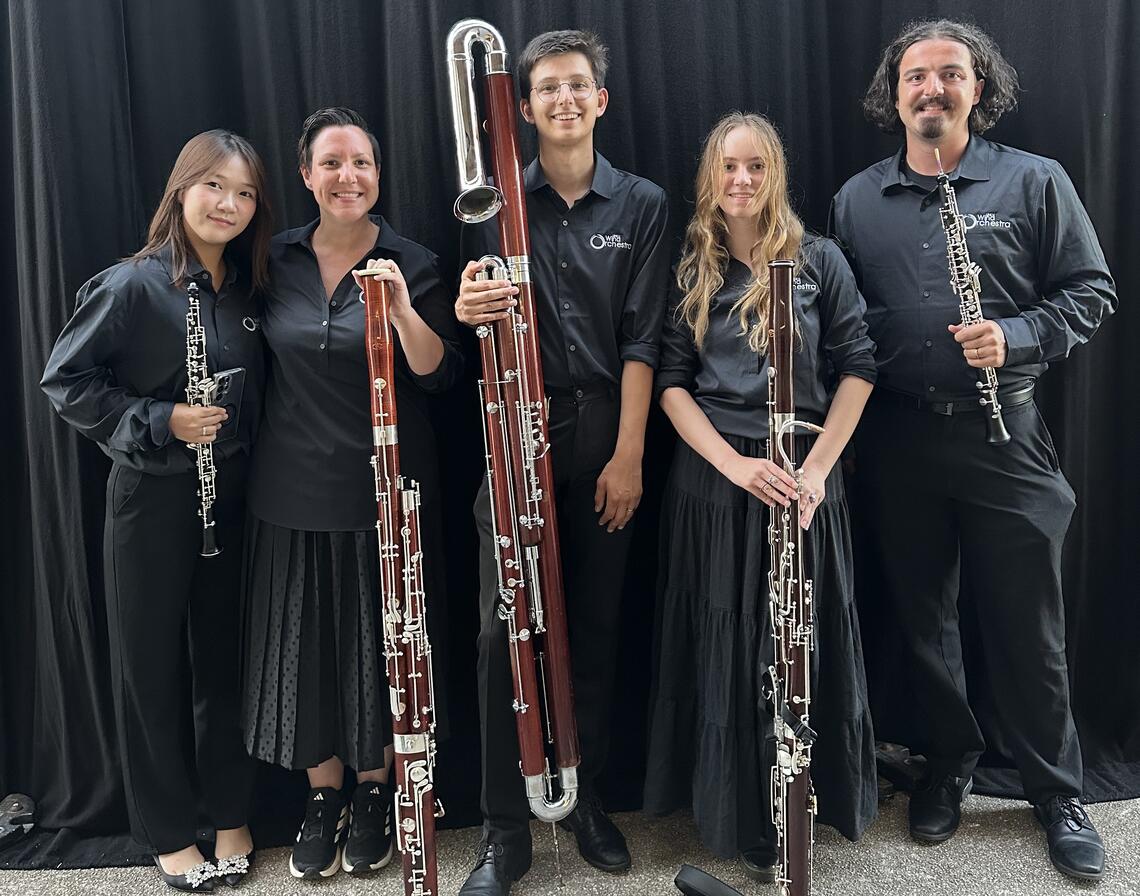 Musicians holding up their bassoons and smiling at the camera