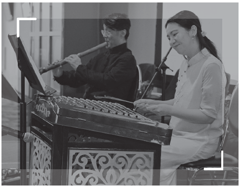 Two musicians perform traditional Chinese music, with a woman playing a yangqin and a man playing a bamboo flute on stage
