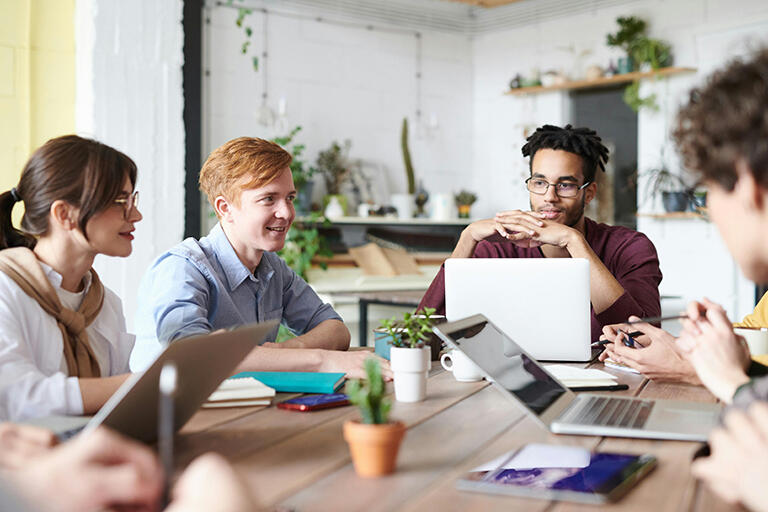 Group of people working together at a table, each with a laptop