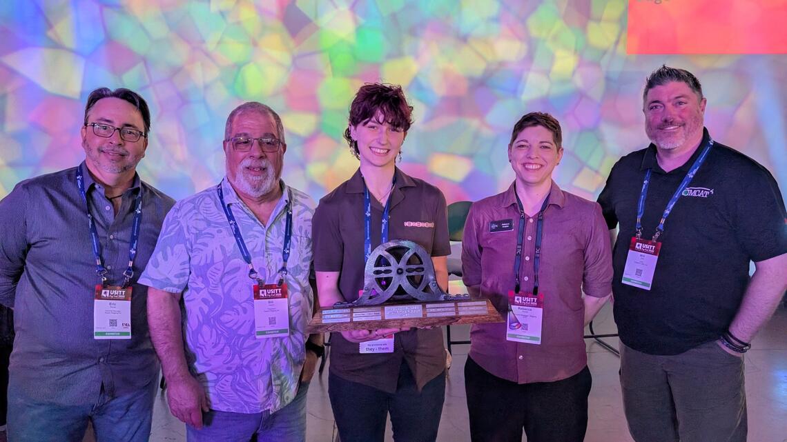 Four persons surrounding a fifth who is holding a large trophy.