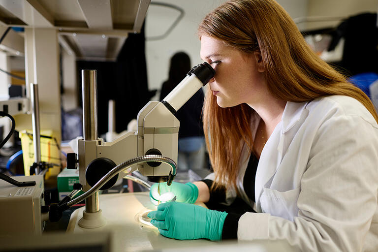 Woman in laboratory clothing looking through a microscope