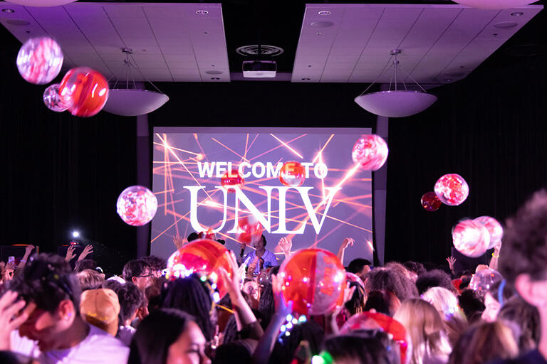 Welcome to U.N.L.V. celebration with many students, a D.J., and red and white balloons bouncing around