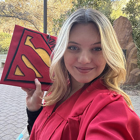 Photo of Grace Ripandelli holding a Supergirl logo grad cap