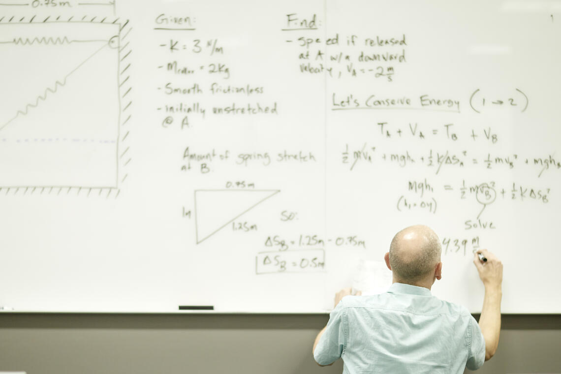 A professor writing formulas on the white board