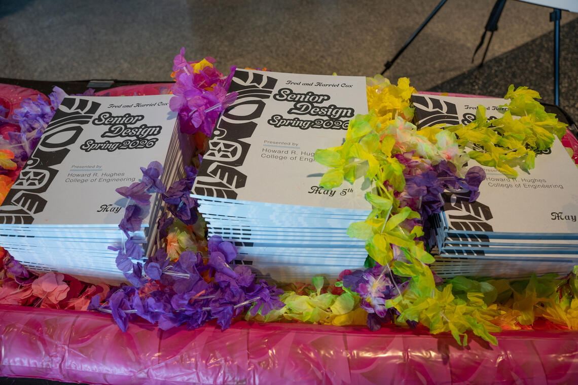 Three stacks of Senior Design booklets surrounded by Hawaiian leis