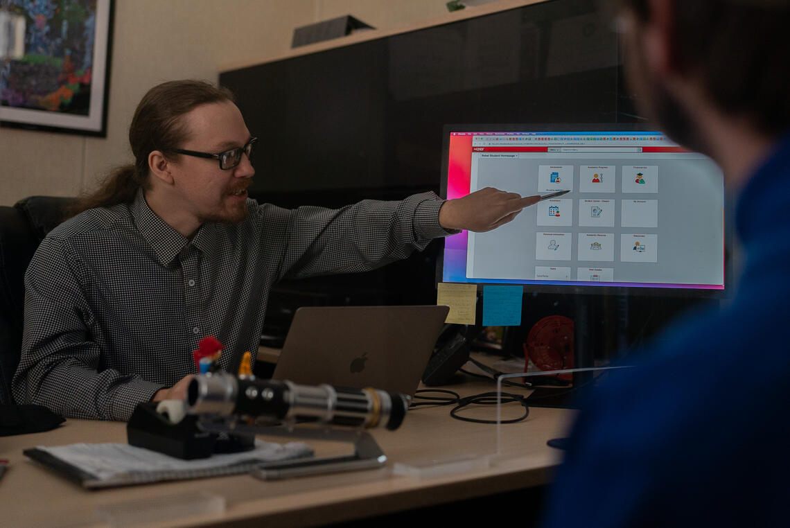 A man in a polo using a pen to point to a computer screen of the "My U-N-L-V" Rebel Student Homepage