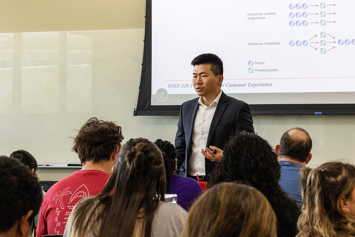 An instructor speaking in front of a classroom with students