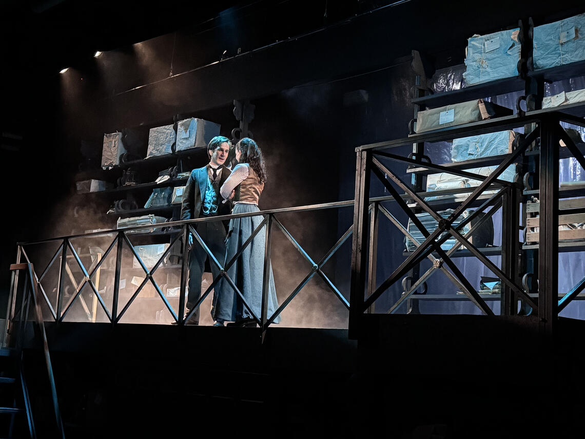Photo of a man and woman in old timey clothes on a stage acting for a play