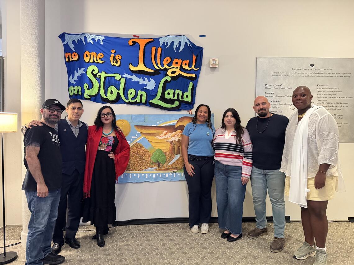 A group of people of all types smiling to the camera as they stand in front of artwork