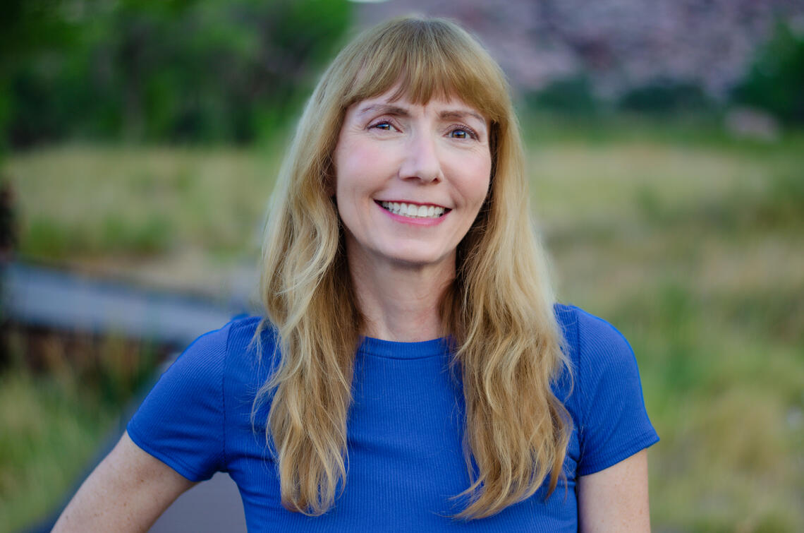 Blonde woman with bangs and a blue shirt smiles to the camera