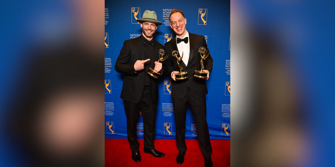Two men on a red carpet holding up Emmy award trophies