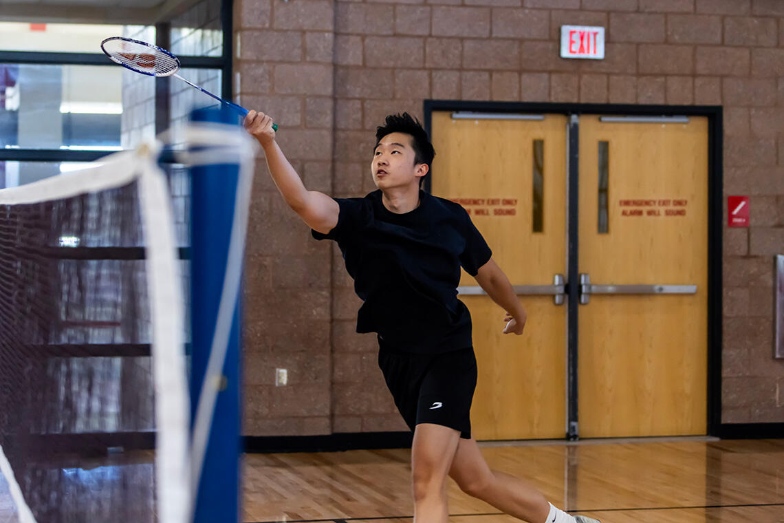 A student reaches to return a shuttlecock during an indoor badminton game