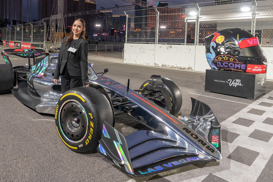 A woman in a black suit poses next to a Formula 1 race car at a race circuit