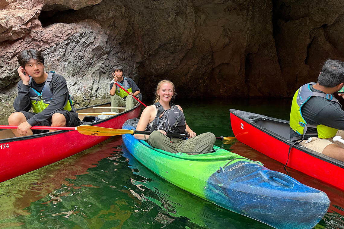 Students wearing life jackets kayak through a cave
