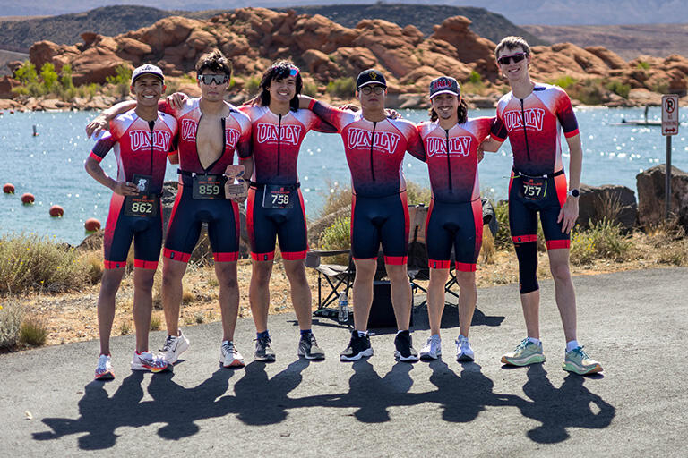 Group of six athletes posing for photo in front of a rocky lake landscape.