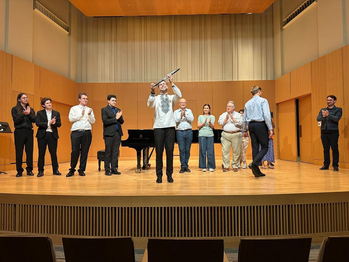 Musicians on stage clapping for someone in the middle of the stage holding up an instrument